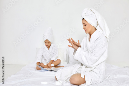 mother in white bathrobes and towels apply cream on hands