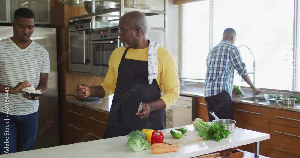 African american senior father and two adult sons standing in kitchen cooking dinner and talking African american senior father and two adult sons standing in kitchen cooking dinner and talking