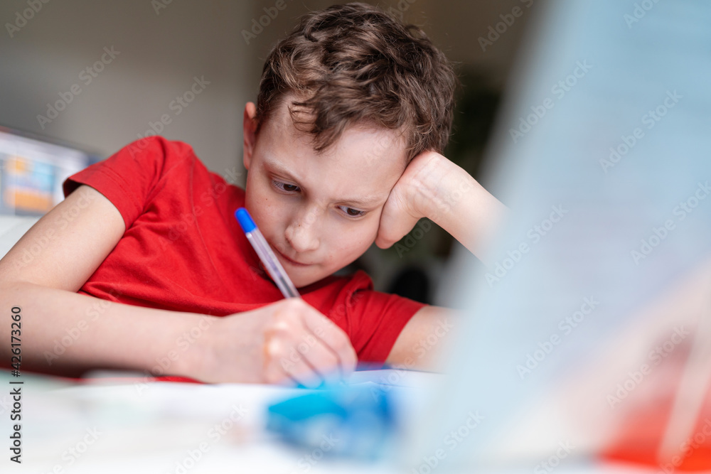 Attentive focused hardworking schoolboy boy sits down at the table and does homework, looks at the textbook, at home. Back to school. The child does math, thinks about the solution of the problem Attentive focused hardworking schoolboy boy sits down at the table and does homework, looks at the textbook, at home. Back to school. The child does math, thinks about the solution of the problem
