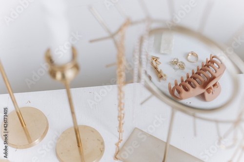 Modern golden accessory and hair clips reflected in boho mirror on white table with vintage candles
