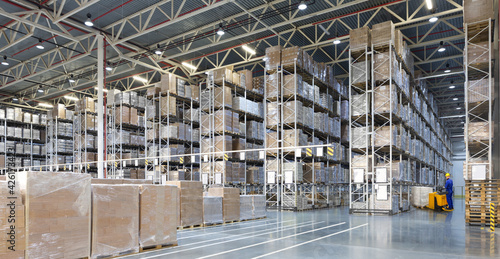 Huge distribution warehouse with high shelves and forklift with young driver.