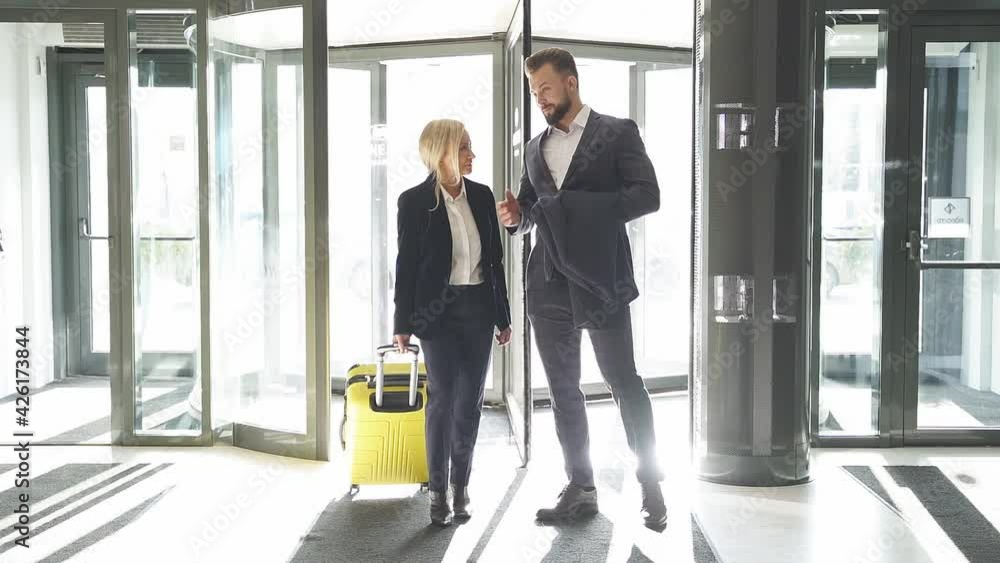 Two business people enter the luxury hotel holding suitcase, caucasian man and woman at business trip. Two business people enter the luxury hotel holding suitcase, caucasian man and woman at business trip.