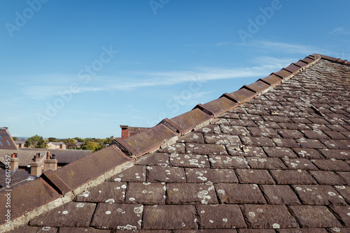 A triangle or hip roof end showing the ridge with capped angle tiles, mortar and lichen on the old traditional stone slates