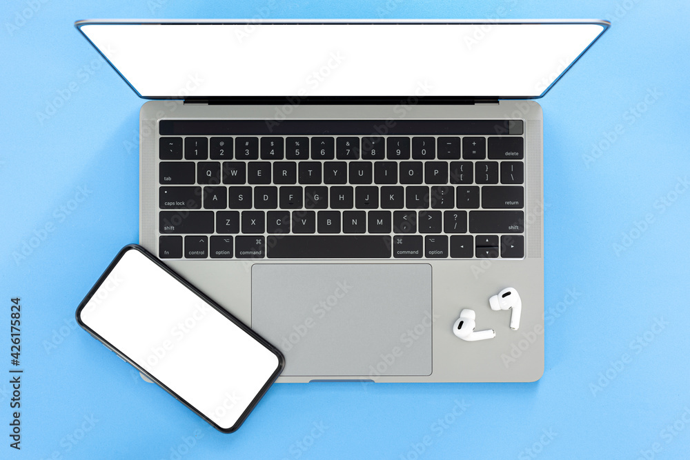 Top view workspace laptop white screen with smartphone and wireless headphones with copy space isolated on blue background Top view workspace laptop white screen with smartphone and wireless headphones with copy space isolated on blue background