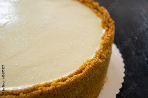 closeup of new york style cheesecake with a thick cookie crust. Black background