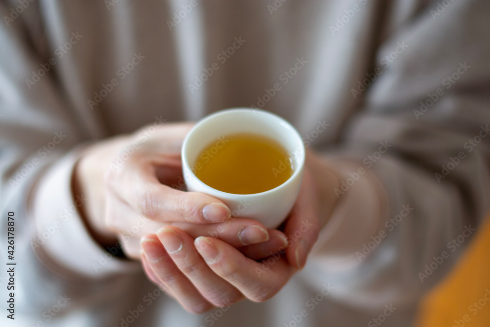 woman holding a small cup of tea with hands. Green tea.  Blurred background selective focus.
