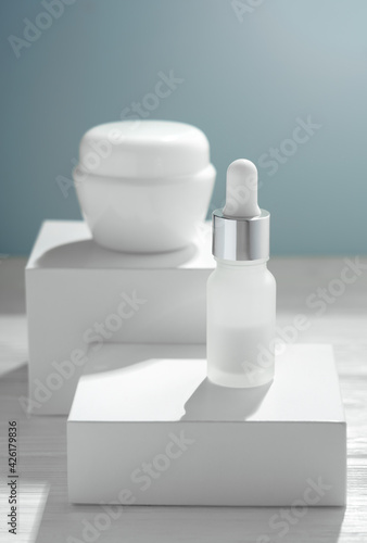 Pipette bottle and cream container on white boxes and blue background