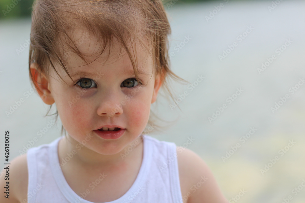 Cute little child kindergarden with gray eyes and short blond hair on a blurred background of a pond Cute little child kindergarden with gray eyes and short blond hair on a blurred background of a pond