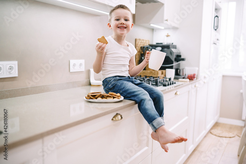 little boy drinking tea with cookies in the kitchen