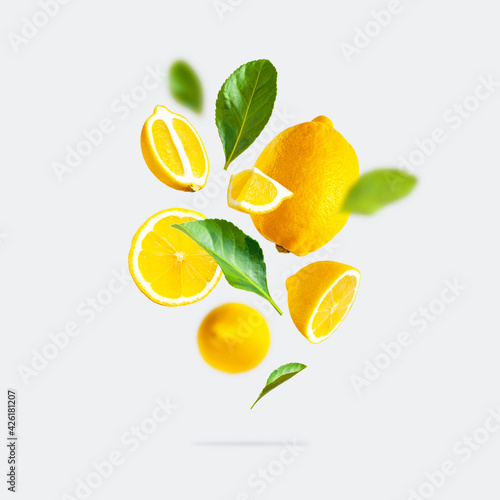 Juicy ripe flying yellow lemons, green leaves on light gray background. Creative food concept. Tropical organic fruit, citrus, vitamin C. Lemon slices. Summer minimalistic bright fruit background photo