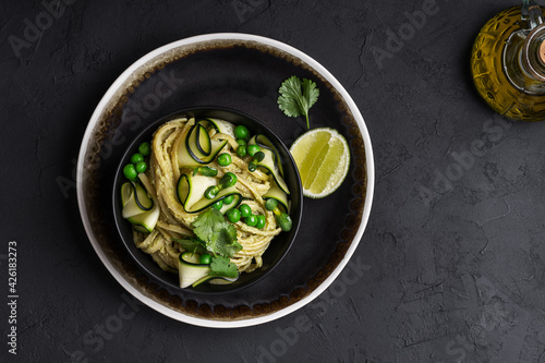 Bowl of linguine pasta with avocado sauce, green peas, zucchini, sprouts on dark grey table