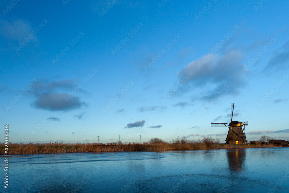 Windmills at Kinderdijk, close to Rotterdam in The Netherlands, in winter with ice on canal at sunset.