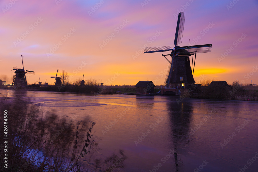 Windmills at sunset in Kinderdijk near Rotterdam in The Netherlands during winter with ice on canal
