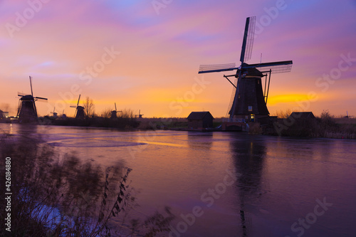 Windmills at sunset in Kinderdijk near Rotterdam in The Netherlands during winter with ice on canal
