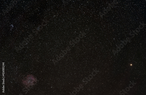 Winter night sky with many stars, Rosette nebula visible in lower left corner,  bright yellow Betelgeuse star on right side