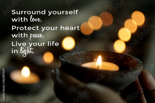 Inspirational motivational quote - Surround yourself with love. Protect your heart with peace. Live your life in light. With person holding a candle light on bokeh candles lights background. photo