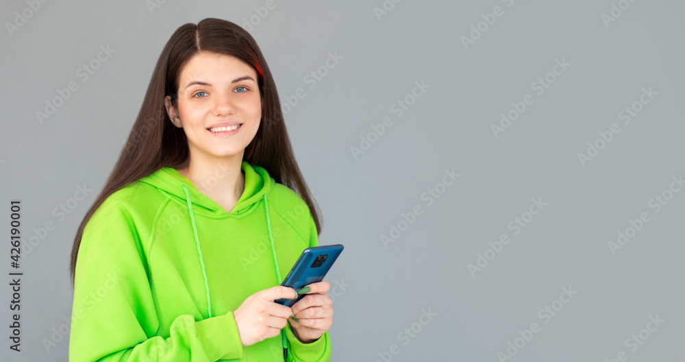 Smiling woman with smartphone in hands looking at the camera over gray background Smiling woman with smartphone in hands looking at the camera over gray background