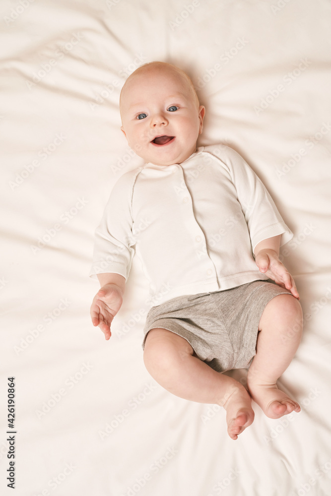 Cute small boy lying at bed. Childhood concept. Light background. Smiling child. Happy emotion. Copyspace. Stay home. Mockup. Children clothes Cute small boy lying at bed. Childhood concept. Light background. Smiling child. Happy emotion. Copyspace. Stay home. Mockup. Children clothes