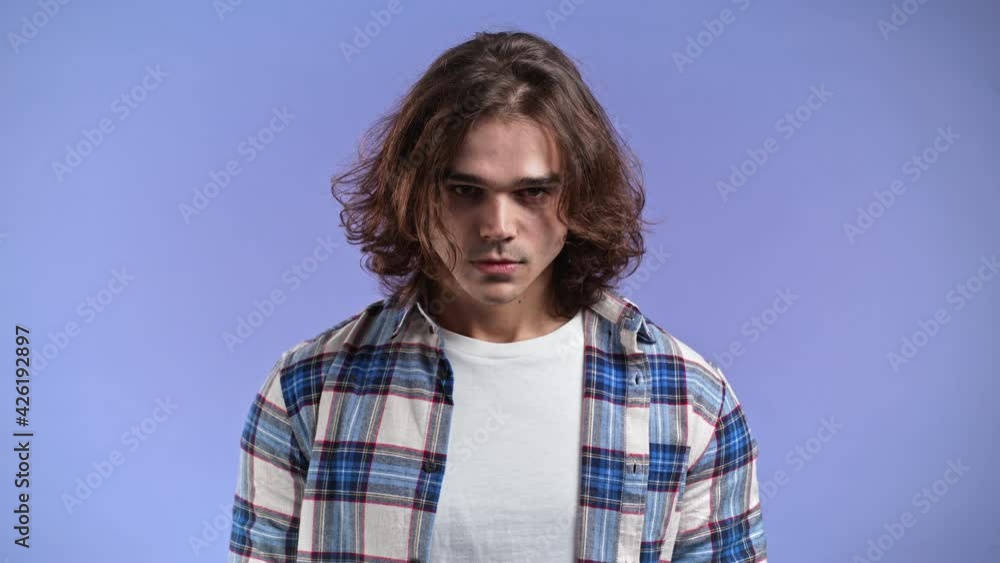 Furious man with long hairstyle on violet background. Guy in stress and rage, he threatens with aggression and looking at camera. Furious man with long hairstyle on violet background. Guy in stress and rage, he threatens with aggression and looking at camera.