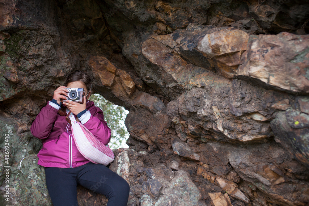 Fototapeta premium Child girl taking pictures from rock shelter