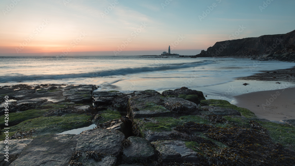 Sunrise view from Old Hartley Bay, Northumberland, England, UK, looking towards St Marys Lighthouse, Whitley Bay and the open sea.