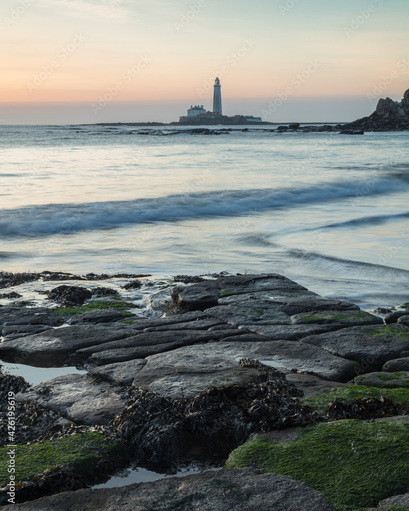 Fototapeta premium Sunrise view from Old Hartley Bay, Northumberland, England, UK, looking towards St Marys Lighthouse, Whitley Bay and the open sea.