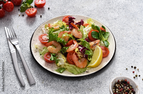 Mix salad with tomatoes and grilled shrimps with sauce and clematis on the kitchen table. Concrete food background.