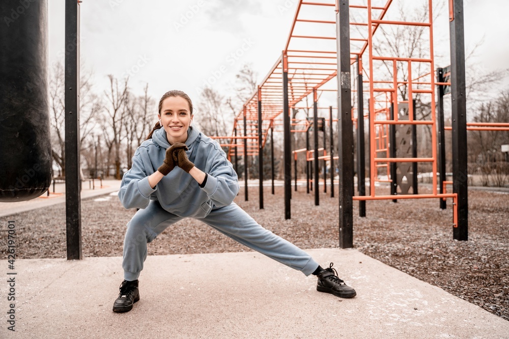 Young woman in sports outfit doing morning workout outdoors. Young female stretching her muscle before running on street sports ground. Staying fit and healthy concept