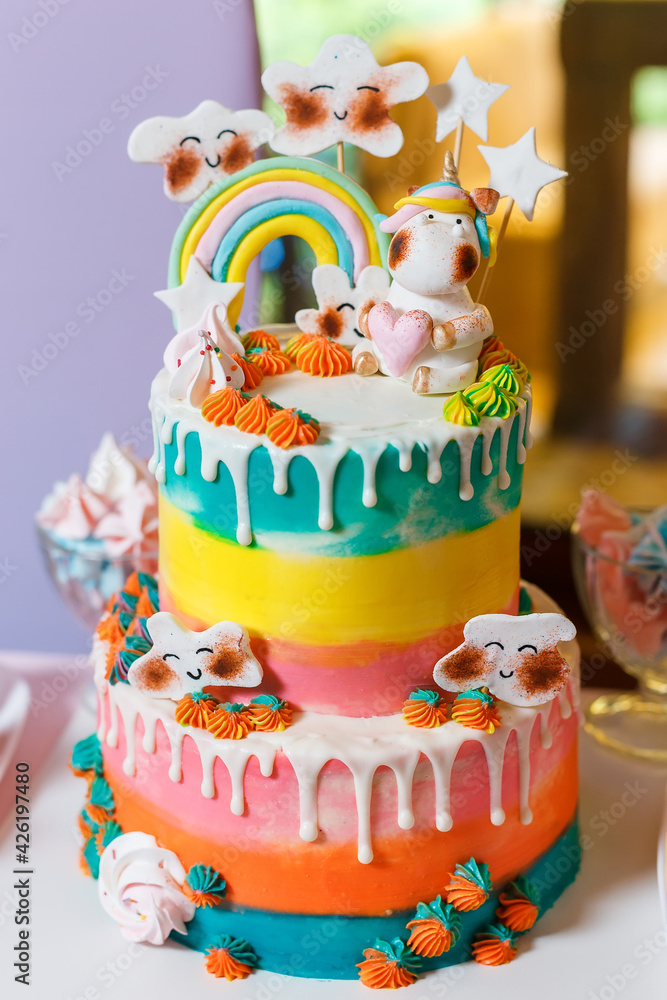 Big cake on the unicorn and rainbow theme. Sweets for children with fantasy style. Multi colored candy bar on birthday party with cupcakes and macaroons Big cake on the unicorn and rainbow theme. Sweets for children with fantasy style. Multi colored candy bar on birthday party with cupcakes and macaroons