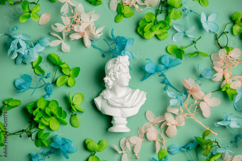 Antique male bust with flowers and leaves on green background. Top view