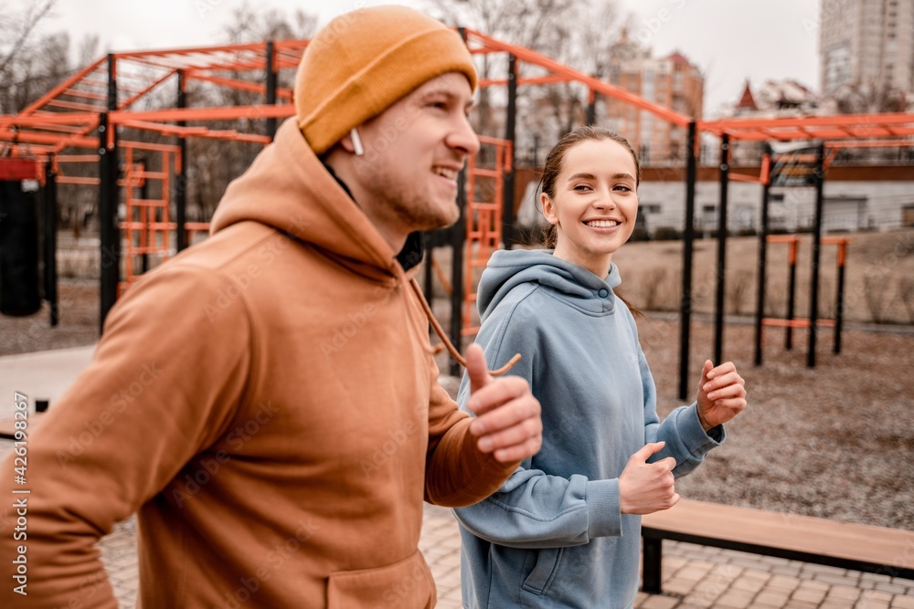 Young man and woman running on street sports ground. Cute couple in sports outfit doing morning workout outdoors. Staying fit and healthy concept