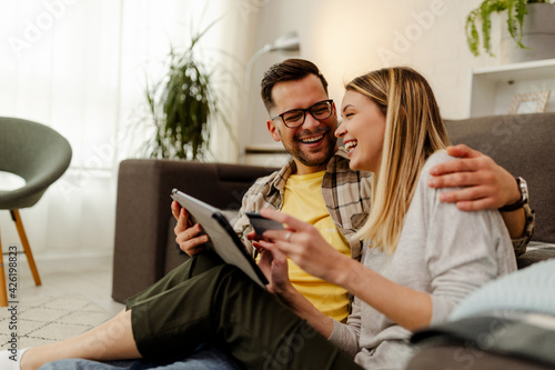 Couple shopping online. Happy couple looking together sitting floor at home.
