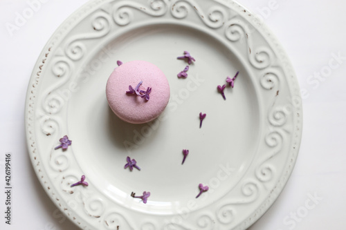 cropped view of woman holding plate with pink delicious French macaroon or macaron with lilac flowers on white background