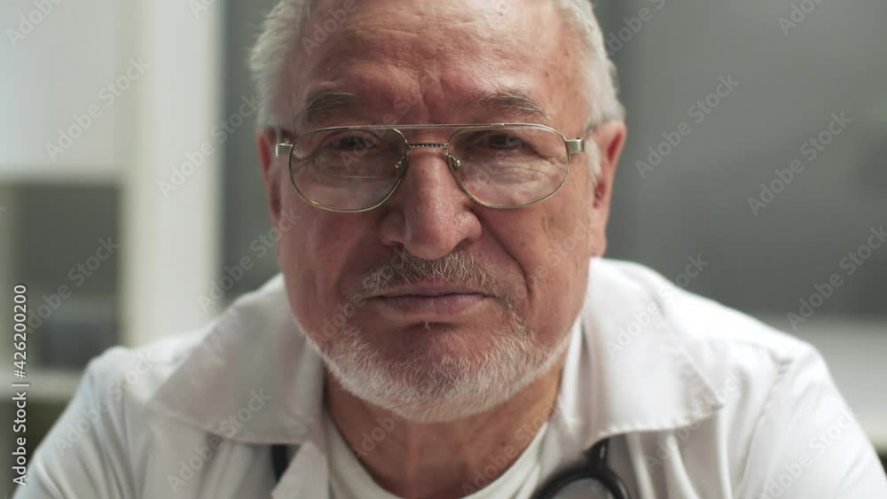 A gray-haired doctor with glasses speaks in close-up and shows a confident gesture with his hands, slow motion A gray-haired doctor with glasses speaks in close-up and shows a confident gesture with his hands, slow motion