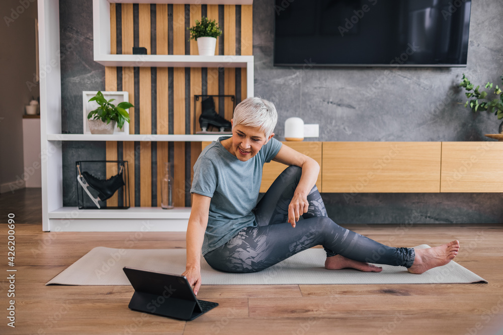 Fit senior woman relaxing at home, sitting on the floor and using tablet.