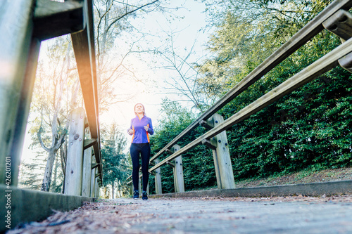 Young beautiful adult woman running down a walkway in a wooded park sport self-care concept at sunset