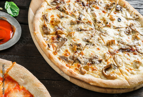 Pizza with chicken meat, mushrooms, cheese, onion, sauce on dark wooden background. Fast food lunch for picnic company, close up, selective focus