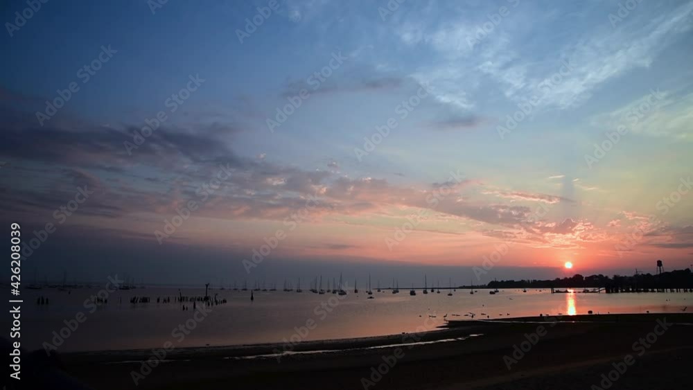 Calm sunrise over Bayshore marina in NJ with warm sunlight and vibrant colors highlighting the sailboats at mooring in the foreground. Calm sunrise over Bayshore marina in NJ with warm sunlight and vibrant colors highlighting the sailboats at mooring in the foreground.