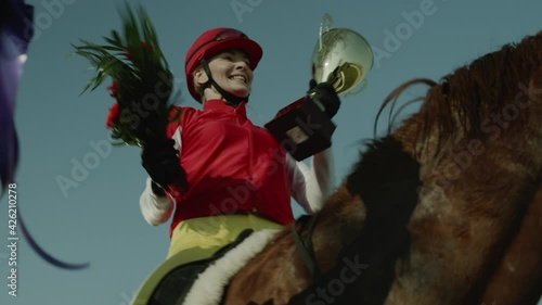 Jockey Woman Celebrate Victory in Race Tournament. Sportswoman Sitting on Horse Horseback, Kissing and Showing Award to Fans. Girl Stallion Rider Happy and Positive Emotion Tracking Shot Slow Motion