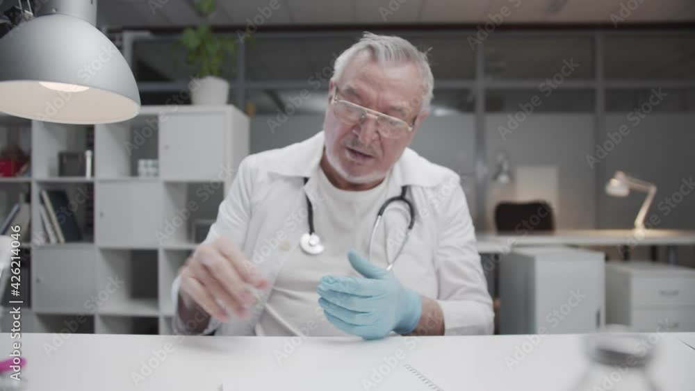 A tired, elderly, experienced doctor nervously removes his latex gloves after a hard days work. Fighting the COVID-19 coronavirus. A tired, elderly, experienced doctor nervously removes his latex gloves after a hard days work. Fighting the COVID-19 coronavirus.