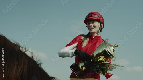 Jockey Sportswoman Horse Race Tournament Winner. Woman in Sportive Uniform Sitting on Horseback Saddle Holding Cup Reward and Flowers. Hippodrome Gamble Sport Winner Tracking Shot Slowmotion