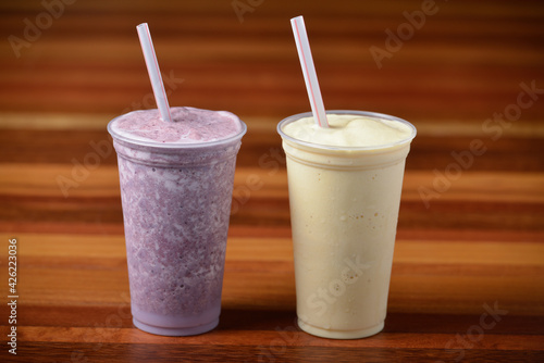 Fruit smoothies in glasses and plastic straws on a dark wooden table.
