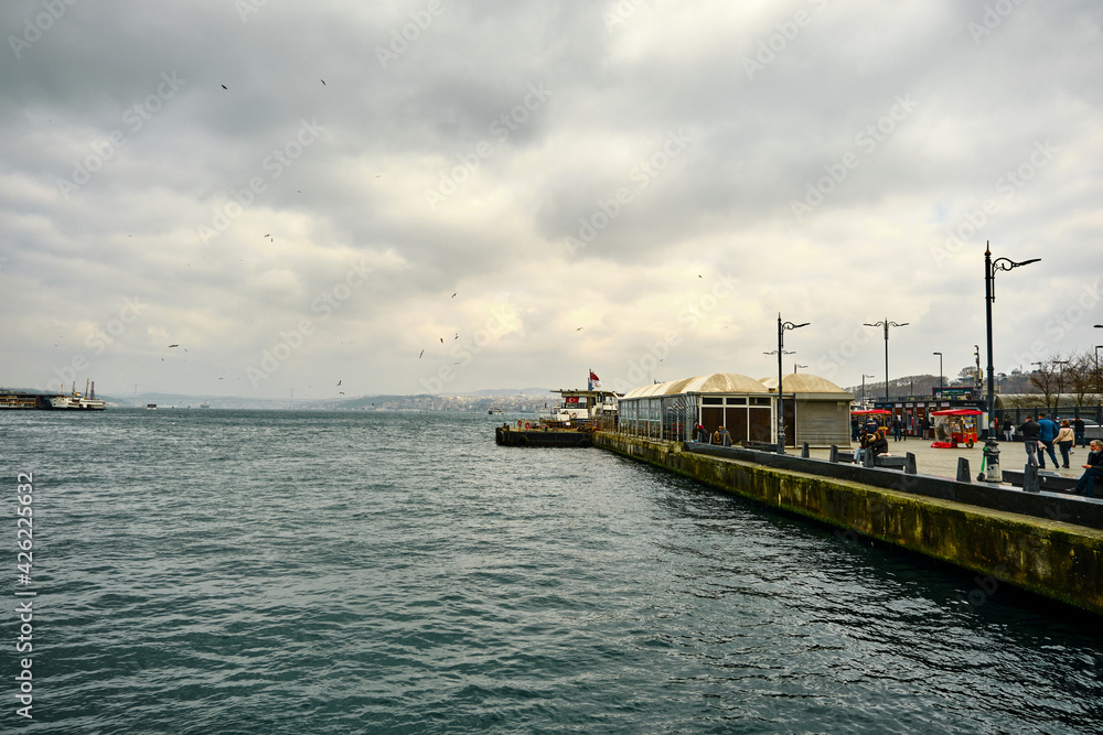 04.03.2021 istanbul Turkey. Eminonu district and shore on bosporus by taking photo from Galata Bridge with people walking on the water's edge during overcast and rainy day.