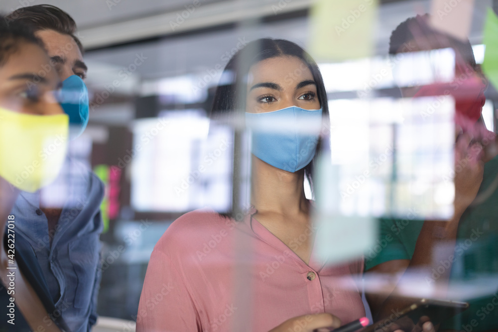 Diverse group of creative colleagues wearing face masks brainstorming in meeting room Diverse group of creative colleagues wearing face masks brainstorming in meeting room