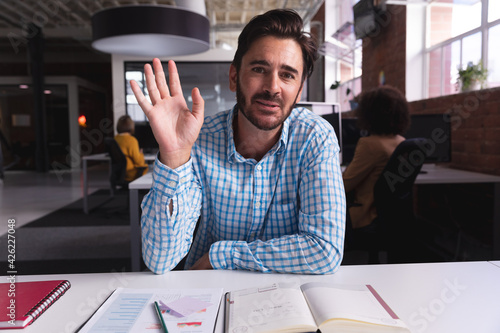Caucasian businessman sitting at desk with documents saying hello having video call