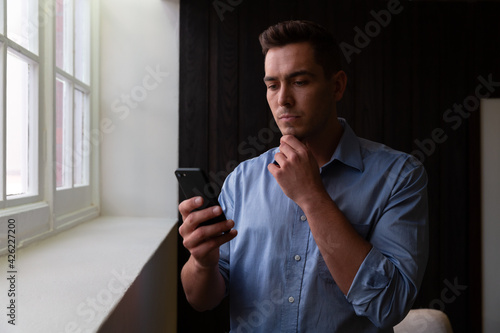 Portrait of stylish caucasian businessman thinking and using smartphone photo