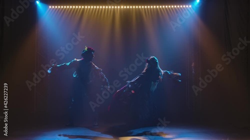 Silhouette couple dancers in romany clothes dancing in dark studio against background of bright lights. Man and woman passionately dancing gypsy dance performing in theatrical show. Slow motion.