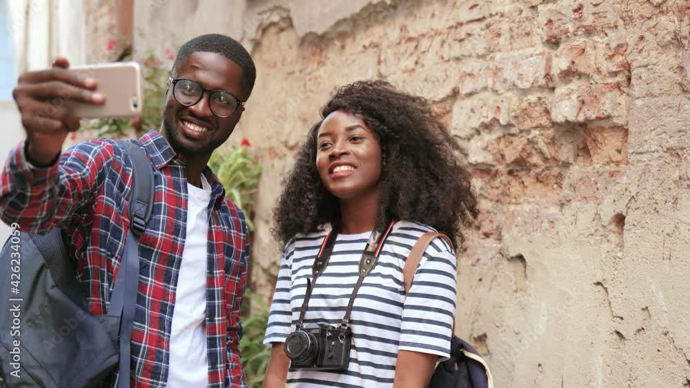Young beautiful african american couple of tourists standing on outside and chatting with friends over video call using smartphone. Young beautiful african american couple of tourists standing on outside and chatting with friends over video call using smartphone.
