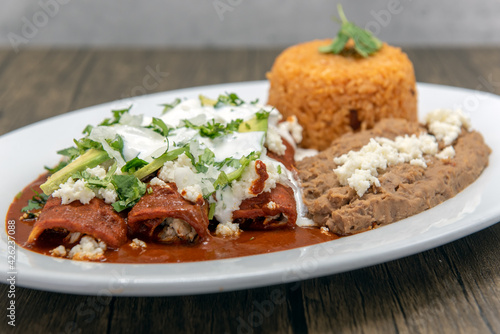 Foto Chicken enchiladas smothered in red sauce served with refried beans and rice for a tasty Mexican food meal