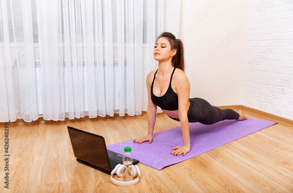 Achieving sound of mind through yoga. Young sporty woman practicing yoga. Woman exercising at home in front of her laptop. Attractive sporty woman practices yoga asana at home. Girl meditating Achieving sound of mind through yoga. Young sporty woman practicing yoga. Woman exercising at home in front of her laptop. Attractive sporty woman practices yoga asana at home. Girl meditating